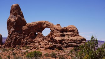 Im Arches Nationalpark erhebt sich ein beeindruckender Felsbogen aus rotem Gestein unter einem strahlend blauen Himmel.