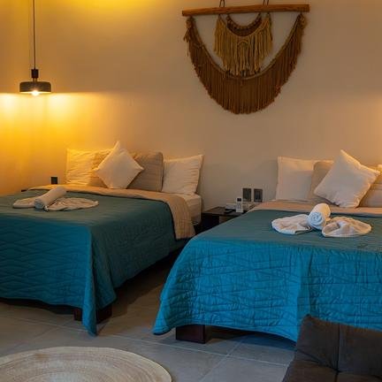Zwei komfortable Betten mit blauen Bettdecken in einem stilvollen Hotelzimmer, sanft beleuchtet von einer Deckenlampe.