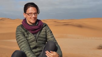 Eine Frau sitzt auf einer Düne in der Wüste - Namibia Reise mit Kindern