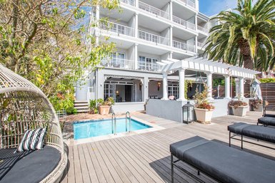 Ein eleganter Außenbereich mit einem kleinen Pool, umgeben von modernen Liegen und üppigem Grün.