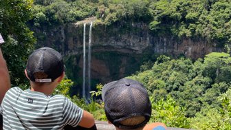 Zwei Kinder stehen an einem Geländer und blicken auf den beeindruckenden Chamarel-Wasserfall in Mauritius.