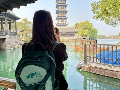 Eine Person mit einem Rucksack steht am Wasser und fotografiert einen historischen Turm in Wuzhen.