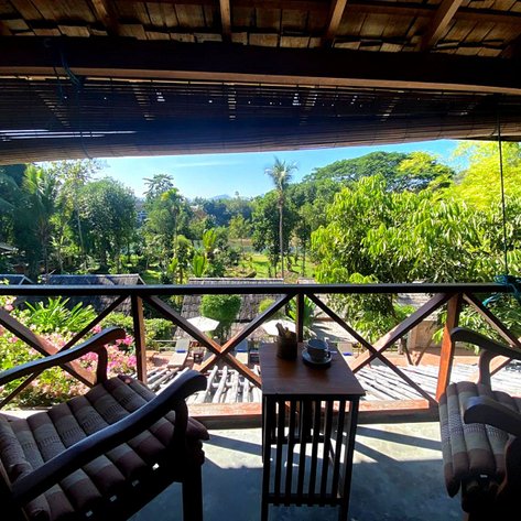 Ein Blick von der Veranda zeigt eine üppige grüne Landschaft mit Palmen und bunten Blumen im Vordergrund.