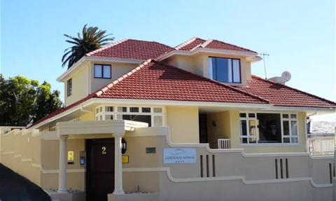 Ein elegantes Haus mit rotem Ziegeldach und großen Fenstern, umgeben von einem gepflegten Garten und Palmen.