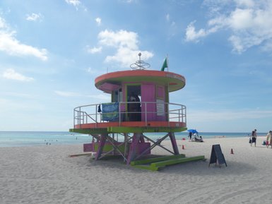 Ein lebhaftes, pinkfarbenes Rettungsschwimmerhaus steht am Strand von Miami, umgeben von feinem Sand und klarem Wasser.