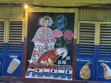 Das Wandgemälde zeigt eine farbenfrohe Darstellung einer mujer in traditioneller panamaischer Tracht zusammen mit einem Papagei.