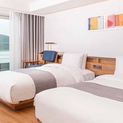 Ein modernes Hotelzimmer mit zwei Einzelbetten, großen Fenstern und Blick auf eine malerische Landschaft.