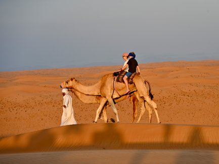 Beduin führt Kamele mit Mutter und Tochter durch die Wüste – Oman Familienreise