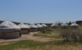Eine Gruppe von Jurten steht in einer trockenen, sandigen Landschaft unter einem klaren blauen Himmel.