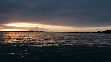 Der Sonnenaufgang über dem ruhigen Wasser der Galapagos-Inseln, mit sanften Wellen und einem dramatischen Himmel.