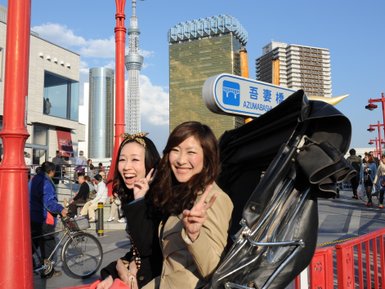 Zwei fröhliche Frauen posieren vor dem Tokyo Skytree, während sie mit den Fingern Peace-Zeichen zeigen.