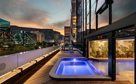 Ein eleganter Balkon mit einem kleinen Pool, umgeben von modernen Gebäuden und einer atemberaubenden Abendkulisse.