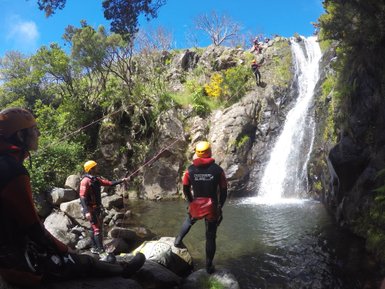 Eine Gruppe von Canyoning-Anfängern steht an einem Wasserfall, bereit, das Abenteuer im klaren Wasser zu beginnen.