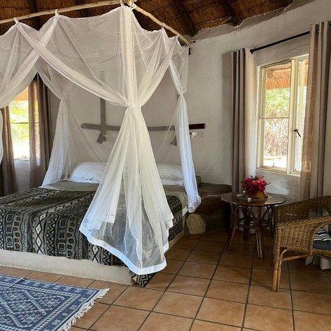 Ein gemütliches Schlafzimmer mit einem großen Bett, umgeben von einem Moskitonetz und einem rustikalen, geflochtenen Stuhl.