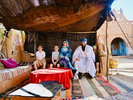 Eine Familie sitzt entspannt unter einem schattigen Zelt in Marokko, umgeben von traditioneller Dekoration und warmem Licht.