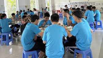 Eine Gruppe von Jugendlichen in blauen T-Shirts sitzt an Tischen und genießt gemeinsam eine Mahlzeit in einem hellen Raum.