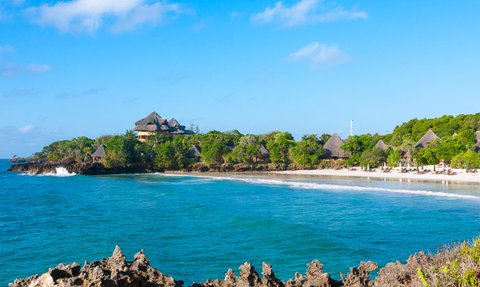 Ein malerischer Blick auf die Küste von Chale Island mit sanften Wellen und üppiger Vegetation im Hintergrund.