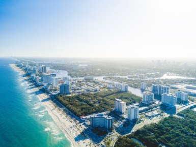 Eine Luftaufnahme zeigt die Küste von Fort Lauderdale mit modernen Gebäuden und dem glitzernden Ozean im Vordergrund.