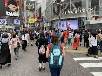 Eine belebte Straße in Shibuya, Tokio, mit vielen Fußgängern und einem großen Starbucks-Schild im Hintergrund.