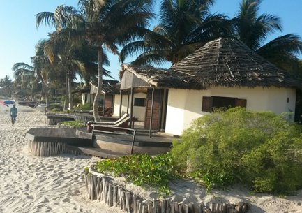 Ein ruhiger Strand mit Palmen und traditionellen Hütten, während Menschen am Ufer spazieren gehen und die Sonne genießen.