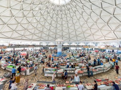Ein belebter Markt mit vielen Menschen, die frische Lebensmittel in einem modernen, kuppelförmigen Gebäude kaufen.