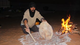 Beduine backt traditionelles Fladenbrot direkt auf dem Wüstensand – Marokko Familienreise