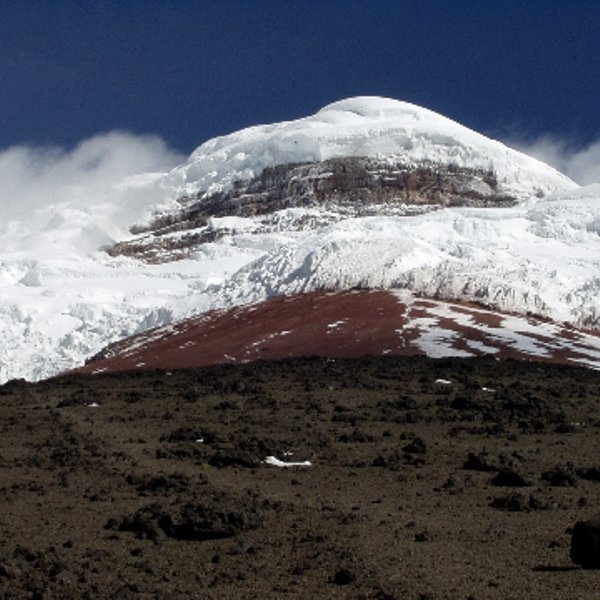 Der majestätische Vulkan Cotopaxi erhebt sich mit schneebedecktem Gipfel über die karge, vulkanische Landschaft.