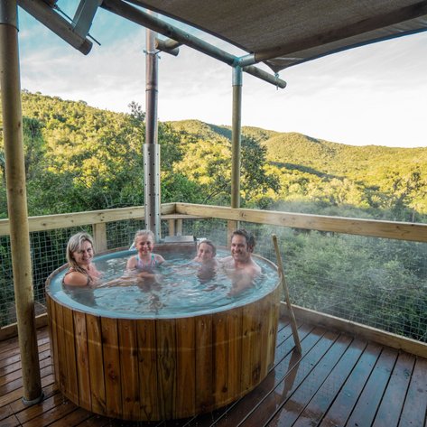 Vier Personen entspannen in einem Holz-Whirlpool mit Blick auf die grüne Landschaft der Eastern Cape.