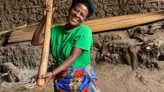 Eine fröhliche Frau in einem grünen T-Shirt mahlt mit einem Holzstößel in einem traditionellen Mörser aus Holz.