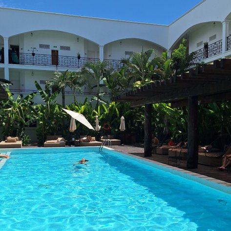 Ein klarer Pool umgeben von üppigem Grün, mit Gästen, die sich entspannen und die Sonne genießen.