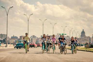 Die Szene zeigt eine Gruppe von Radfahrern, die in der urbanen Kulisse von Havanna unterwegs sind.