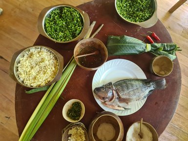 Ein Tisch voller frischer Zutaten für ein Kochkurs, darunter Fisch, Kräuter und Gewürze, die zum Kochen einladen.