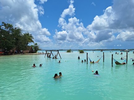 Eine Gruppe von Menschen schwimmt in einem türkisfarbenen Gewässer unter einem strahlend blauen Himmel mit weißen Wolken.