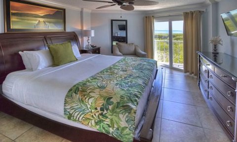 Ein geräumiges Hotelzimmer mit einem großen Bett, dekoriert mit einem grünen Blattmuster und Blick auf das Meer.