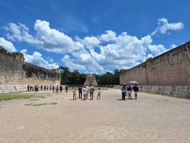 Besucher erkunden die beeindruckenden Ruinen von Chichen Itza unter einem strahlend blauen Himmel mit weißen Wolken.