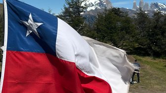 Die chilenische Flagge weht vor einer beeindruckenden Berglandschaft mit schneebedeckten Gipfeln im Hintergrund.