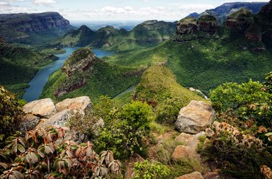 Ein atemberaubender Blick auf grüne Berge und einen glitzernden Fluss, umgeben von üppiger Vegetation und Felsen.