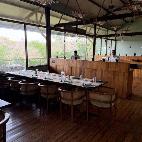 Ein stilvolles Restaurant mit Holzmöbeln und großen Fenstern, die einen Blick auf die grüne Umgebung bieten.