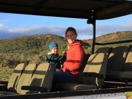 Mutter und Kind genießen gemeinsam die Safari im offenen Jeep und lächeln in die Kamera – Garden Route Reise mit Kindern