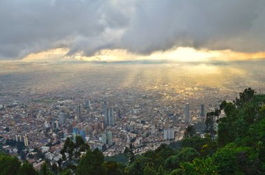 Ein atemberaubender Blick auf Bogotá, umgeben von Wolken, mit Sonnenstrahlen, die die Stadt erleuchten.