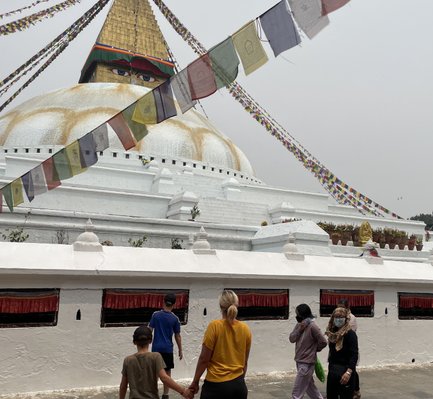 Eine Familie mit zwei Kindern erkundet den Bodhnath Stupa, umgeben von bunten Gebetsfahnen und einer spirituellen Atmosphäre.