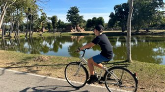 Junge fährt mit Fahrrad durch die Anlage von Wat Mahathat in Sukhothai - Thailand Familienreise