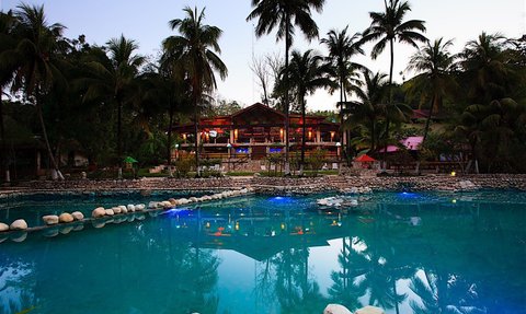 Ein malerisches Resort mit einem klaren Pool, umgeben von Palmen und einer einladenden Holzstruktur im Hintergrund.