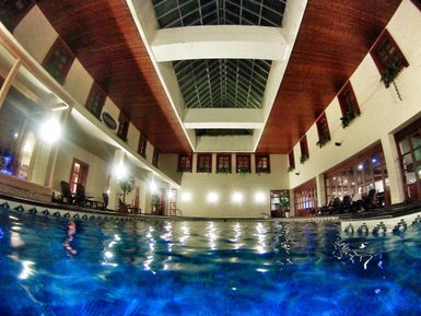 Ein Innenpool mit klarem Wasser, umgeben von großen Fenstern und einer hohen Decke, die mit Holz verkleidet ist.