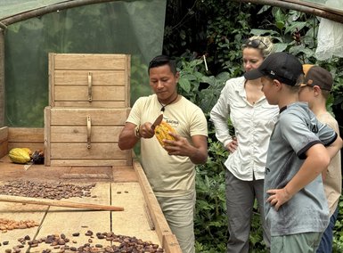 Ein Mann schneidet eine Kakaofrucht auf, während eine Gruppe von Kindern und einer Frau aufmerksam zuschaut.