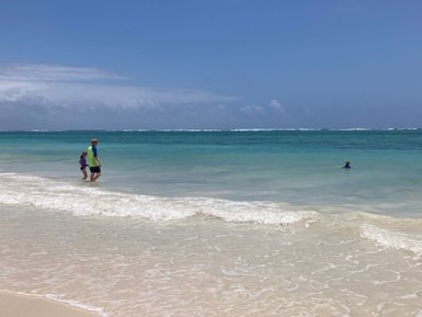 Zwei Kinder gehen am Strand entlang, während die Wellen sanft an den Ufer schlagen und der Himmel strahlend blau ist.