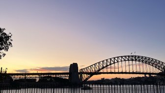 Im Vordergrund erstreckt sich ein grünes Feld, während die beeindruckende Sydney Harbour Bridge sich majestätisch im Hintergrund erhebt.