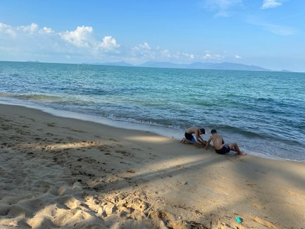 Zwei Jungen spielen am Strand, während die Wellen sanft an den Sand schlagen und die Sonne am Himmel scheint.