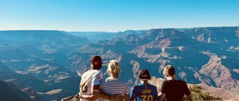 Eine Gruppe von vier Personen sitzt am Rand des Grand Canyon und genießt die atemberaubende Aussicht auf die Landschaft.