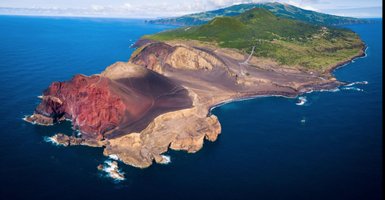 Eine beeindruckende Küstenlandschaft mit roten Klippen, die ins tiefblaue Wasser des Ozeans fallen.